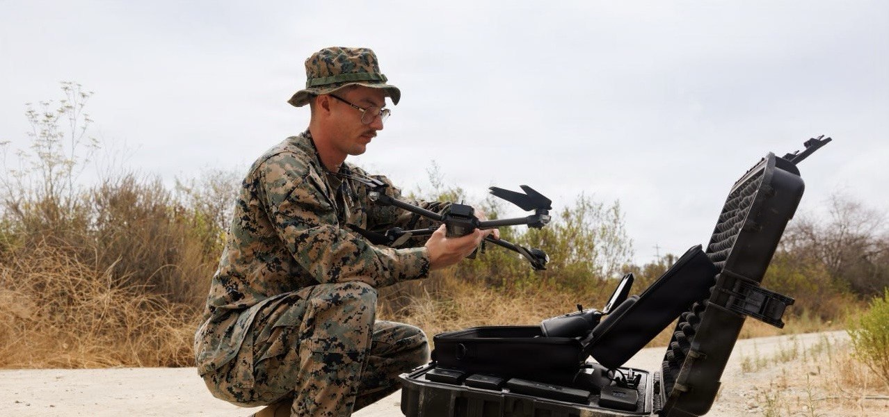 A U.S. Marine in uniform conducts a pre-flight check on a SKYDIO X2D drone in an outdoor field at Marine Corps Base Camp Pendleton